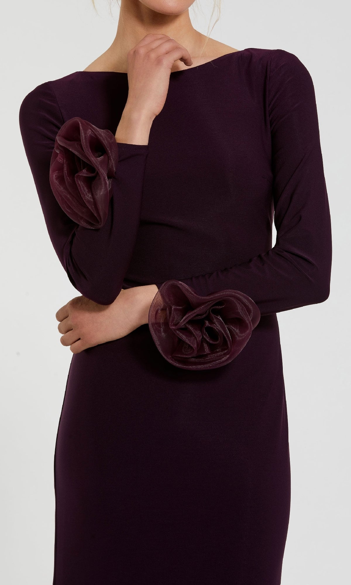 A person poses in the Mac Duggal 49949 long sleeve formal dress, a dark purple gown with ruffled sleeve accents, crossing one arm over their body and touching their face with the other hand.